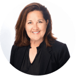 Professional headshot of a smiling woman with shoulder-length brown hair, wearing a black blazer and a black blouse, set against a light green background.